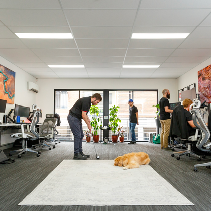 a man is playing golf in an office while a dog lays on the floor